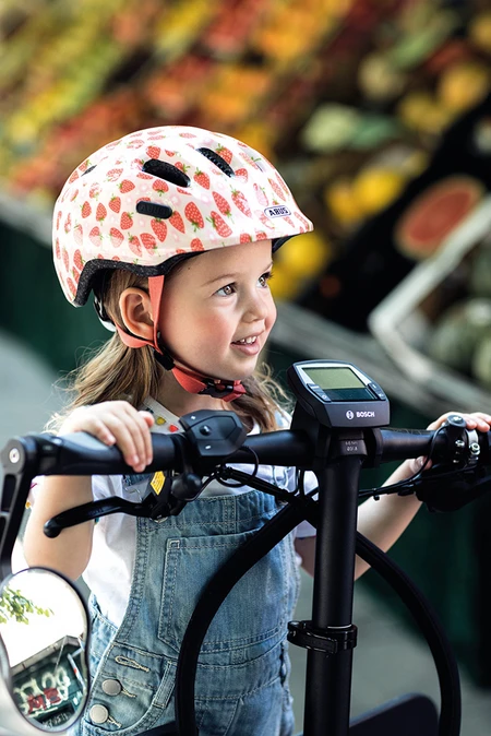 Kleines M&auml;dchen mit dem Smiley 2.1 Kinderhelm Strawberry Rose auf Fahrrad.